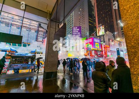 Menschen und Verkehr, die durch den beleuchteten, strahlenden und treibenden Dampf an der Kreuzung nahe dem Times Square in einer Schneesturmnacht fahren, Stockfoto