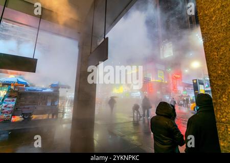 Menschen und Verkehr, die durch den beleuchteten, strahlenden und treibenden Dampf an der Kreuzung nahe dem Times Square in einer Schneesturmnacht fahren, Stockfoto