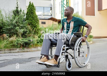 Ganzkörperporträt eines aktiven afroamerikanischen Mannes mit Behinderung, der sich auf Betonpflaster in grüner Stadtlandschaft bewegt Stockfoto