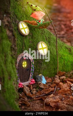 Ein bezauberndes Märchenhaus, eingebettet in die moosigen Wurzeln eines Baumes in einem Wald, mit einer kleinen skurrilen Tür mit einem roten Stern, umgeben von winzigen Fenstern Stockfoto