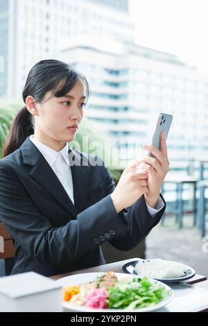 Eine junge Frau, die einen Anzug trägt und ein Smartphone hält, das in einem Büroblock isst Stockfoto