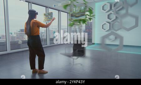 Die talentierte asiatische Designerin in Augmented-Reality-Headsets nutzt Virtual Interior Design Software, um stilvolle Wohnungen oder Büroräume mit 3D-Möbeln und -Ausstattung zu arrangieren. Futuristische VFX-Animation. Stockfoto