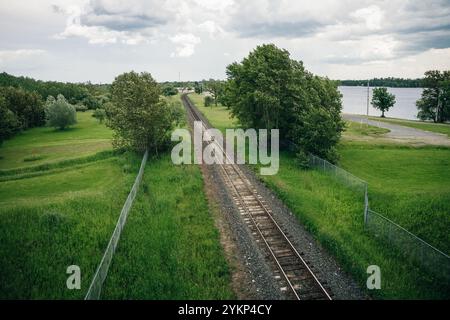 Die Luftaufnahme einer Drohne zeigt Bahngleise, die sich durch üppige Felder und dichte Wälder schlängeln. Die Schienen, die im Sonnenlicht leuchten, bilden einen schlanken Weg. Hg Stockfoto