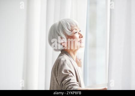 Seniorin öffnet Vorhänge Stockfoto