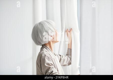 Seniorin öffnet Vorhänge Stockfoto