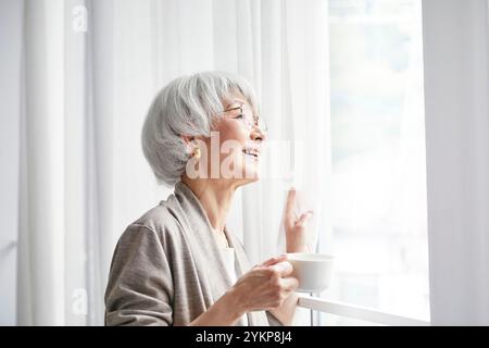Seniorin öffnet Vorhänge Stockfoto