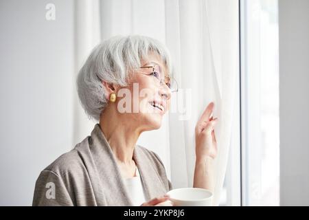 Seniorin öffnet Vorhänge Stockfoto