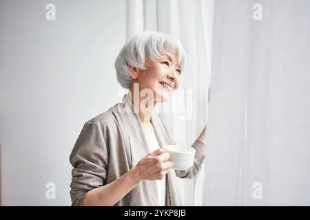 Seniorin öffnet Vorhänge Stockfoto
