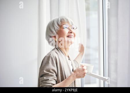 Seniorin öffnet Vorhänge Stockfoto