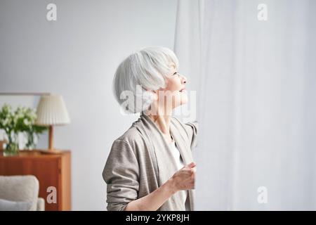 Seniorin öffnet Vorhänge Stockfoto