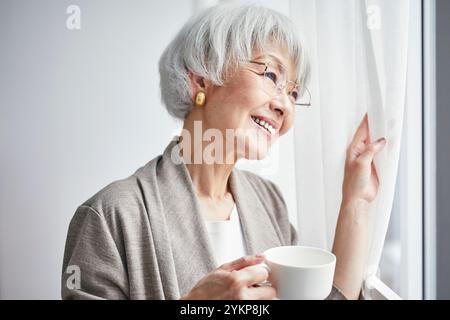 Seniorin öffnet Vorhänge Stockfoto