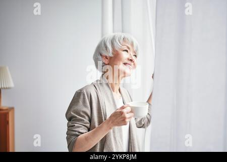 Seniorin öffnet Vorhänge Stockfoto