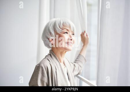 Seniorin öffnet Vorhänge Stockfoto