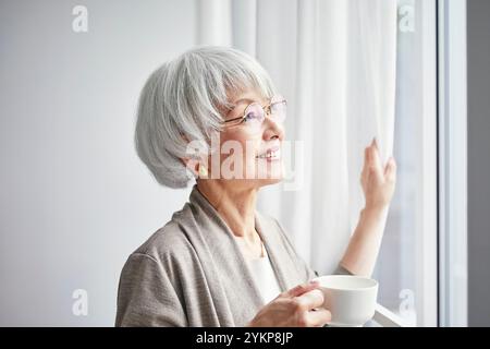 Seniorin öffnet Vorhänge Stockfoto