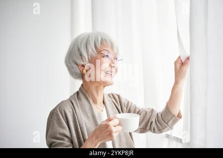 Seniorin öffnet Vorhänge Stockfoto