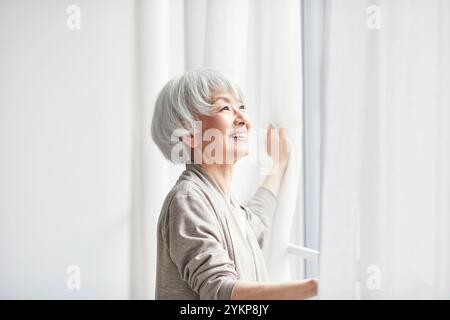 Seniorin öffnet Vorhänge Stockfoto