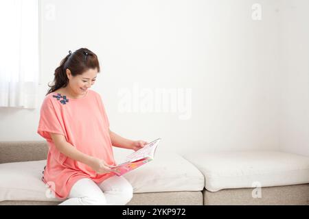 Schwangere Frau, die auf dem Sofa sitzt und eine Zeitschrift liest Stockfoto