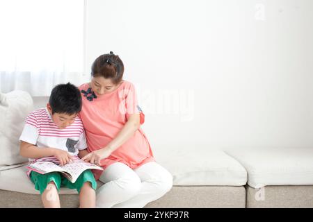 Schwangere Mutter und Grundschulkinder sitzen zusammen auf einem Sofa, schauen sich eine Zeitschrift an und führen ein Gespräch Stockfoto