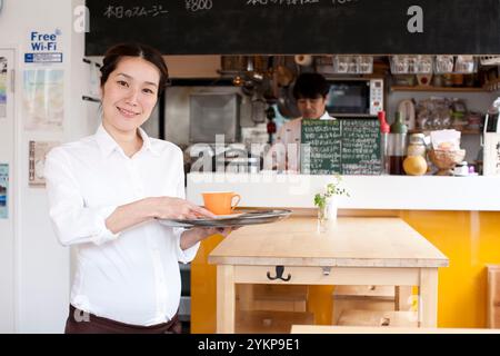 Schwangere Frau lächelt und serviert in einem Restaurant mit einer Tasse Kaffee in der Hand Stockfoto