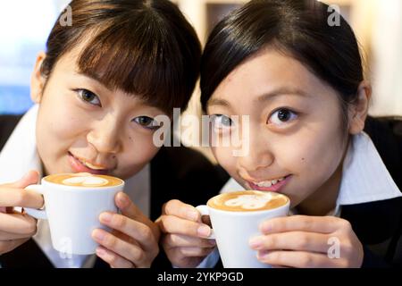 Zwei Frauen in Anzügen trinken Kaffee mit viel Milchschaum an einer Cafétheke. Stockfoto