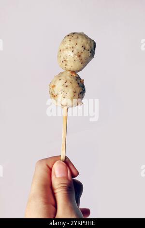 Japanischer Oden schwarzer Pfeffer Fischball, Hühnchen Fleischbällchen, isolierter weißer Fleischbällchen köstlich lecker. Hand hält Fischkugel auf Stock Seafood Street Food Stockfoto