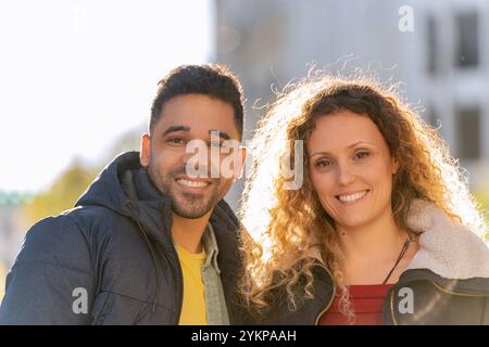 Fröhliches Multi-Ethno-Paar, das einen sonnigen Tag in der Stadt genießt und in ihren stilvollen Winteroutfits Glück und Zweisamkeit ausstrahlt Stockfoto