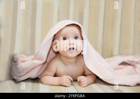 Ein entzückendes Baby blickt staunend auf, während es von einer weichen rosafarbenen Decke bedeckt ist, die gemütlich ist Stockfoto