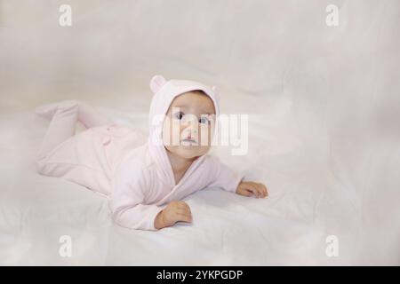 Ein entzückendes, niedliches Baby, gekleidet in einem kuscheligen pinken Pyjama, liegt friedlich auf einer flauschigen, weichen Decke Stockfoto