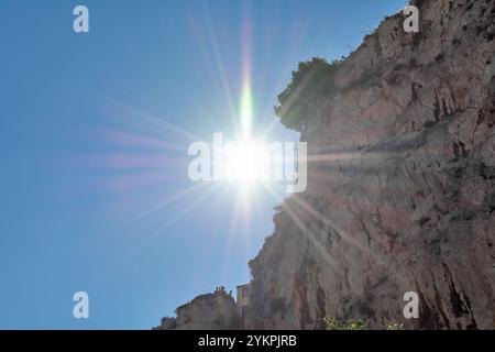 Ein atemberaubender Blick auf die Sonne, die hell über einer zerklüfteten Klippe scheint, mit Lichtstrahlen, die sich über einen klaren blauen Himmel ausbreiten und eine dramatische und captiva erzeugen Stockfoto