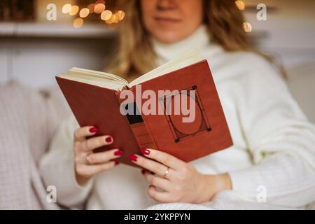 Ein Mädchen sitzt im Winter in warmweißen Kleidern zu Hause und liest ein Buch Stockfoto