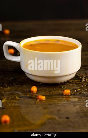 Tee mit Sanddorn in einem weißen Becher, Zubereitung von grünem Tee mit reifem orangenem Sanddorn, Nahaufnahme Stockfoto