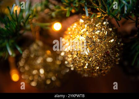 Nahaufnahme eines glitzernden goldenen Weihnachtsschmucks, der an einem Baumzweig hängt, mit sanften leuchtenden Lichtern, die festliche Feiertagsatmosphäre einfangen. Ide Stockfoto