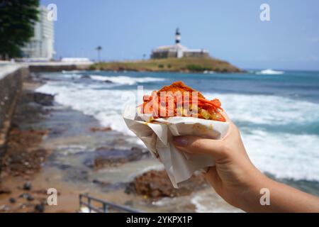 Acaraje in Salvador de Bahia, Brasilien. Brasilianisches traditionelles Gericht Acaraje Street Food aus dem Nordosten Brasiliens mit Farol da Barra Lighthouse und Bay of A Stockfoto