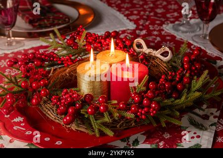 Ein lebendiger Weihnachtstisch mit leuchtenden Kerzen, umgeben von einem üppigen Beerkranz. Das elegante Dekor schafft eine warme Atmosphäre. Stockfoto