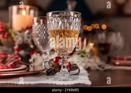 Ein wunderschöner festlicher Tisch mit einem Kristallglas gefüllt mit goldener Flüssigkeit, umgeben von Kerzen und Weihnachtsdekor. Stockfoto