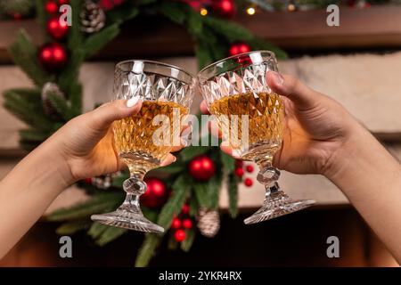 Zwei Hände halten Kristallgläser gefüllt mit Sekt vor Weihnachtsdekorationen und Lichtern, was eine warme und festliche Atmosphäre schafft. Stockfoto