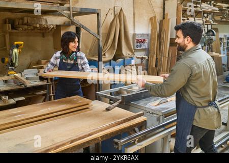 Zwei Arbeiter, ein jüngerer Mann und eine ältere Frau, arbeiten in einem belebten Holzhof zusammen. Sie behandeln Holzdielen zusammen, zeigen Teamwork und Stockfoto