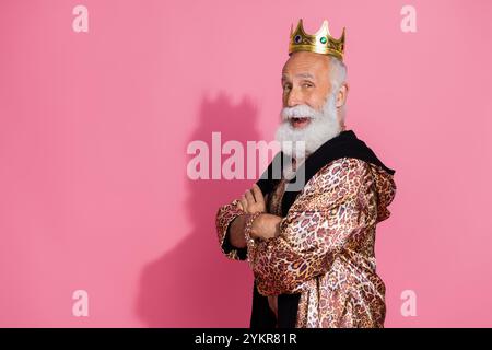 Profilporträt des reichen alten Königs überkreuzte Arme goldene Krone Leopardenmantel leerer Raum isoliert auf rosa Hintergrund Stockfoto