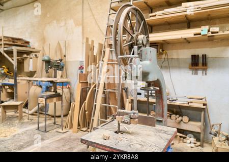 Eine Vintage-Holzbearbeitungsmaschine steht zwischen Werkzeugen und Holzbrettern in einer sauberen und organisierten Holzwerkstatt, die Handwerkskunst und Aufmerksamkeit widerspiegelt Stockfoto