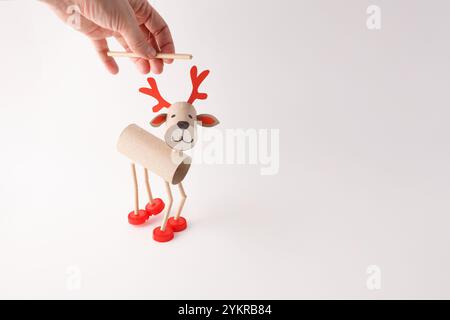 DIY-Rentierpuppe aus Pappröhrchen, roten Kunststoffkappen und Papierdetails. Studio auf weißem Hintergrund. Feiertagsbasteln und Dekoration Konz Stockfoto