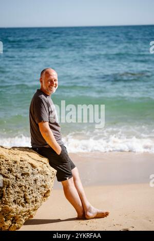 Kaukasischer Mann sitzt auf einem Felsen am São Rafael's Beach in Albufeira, Algarve - Portugal Stockfoto