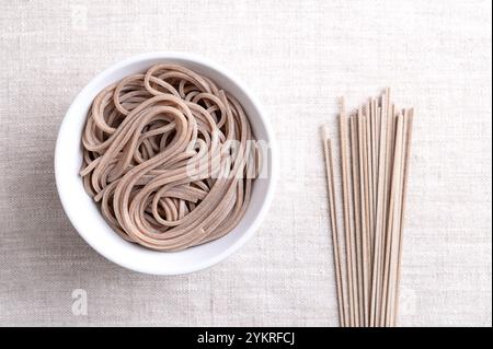 Gekühlte, gekochte Soba-Nudeln in einer weißen Schüssel auf Leinenstoff. Dünne japanische Nudeln, die hauptsächlich aus Buchweizenmehl hergestellt werden, wobei Weizenmehl gemischt wird. Stockfoto