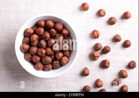 Haselnusskerne, auch bekannt als Kopfnüsse und Filberts, in einer weißen Schüssel auf Leinen. Ganze, getrocknete und geschälte Nüsse, Früchte des Haselnussbaums Corylus avella Stockfoto