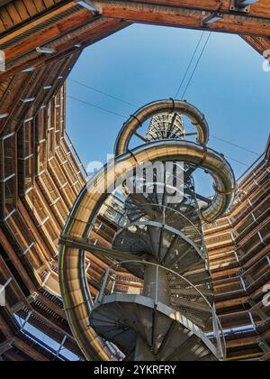 Eine hoch aufragende Wendeltreppe mit einer Metallrutsche schlängelt sich in einem Holzbau nach oben und führt zu einem offenen Himmel. Das architektonische Design. Stockfoto