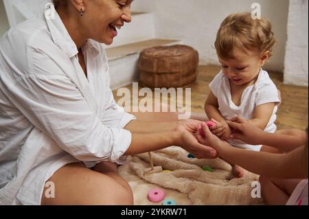 Eine fröhliche Mutter und ihr Kind teilen einen verspielten Moment auf dem Boden mit farbenfrohen Spielzeugen, die eine warme Familienverbindung fördern. Dies fängt das Wesen von ein Stockfoto