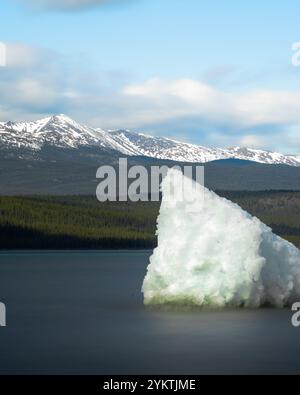 Ein kleiner Eishaufen mitten in einem blauen, unberührten See mit Blick auf Berge und Wälder im Hintergrund. Yukon Territory, Nordkanada. Stockfoto