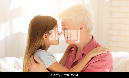 Liebliches kleines Mädchen und ihre Oma berühren Nasen und umarmen sich zu Hause Stockfoto