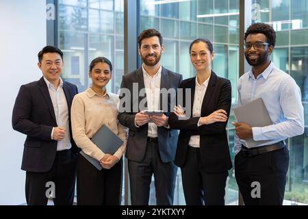 Gruppe von fünf verschiedenen Geschäftsleuten, die selbstbewusst in der Büroumgebung stehen. Teammitglieder, die Ordner und Telefone halten, zeigen Einheit, Teamwork, Professionalität und Vielfalt. Stockfoto