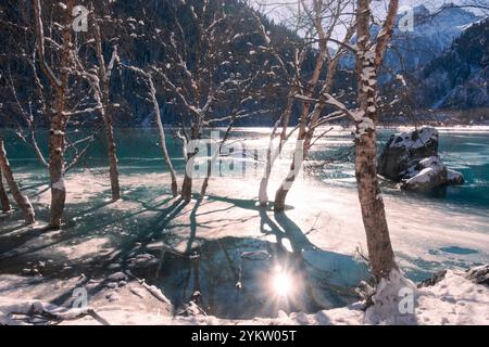 Ein wunderschöner Wintersee in den Bergen, umgeben von einem Fichtenwald, ist an einem sonnigen und frostigen Tag bereits gefroren. Lake Issyk Almaty Kasachst Stockfoto