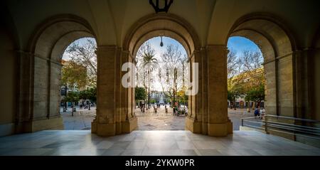 Sevilla, Spanien, 28. Januar 2021, Ein malerischer Blick unter dem bogenförmigen Portikus des Rathauses von Sevilla, der die pulsierende plaza mit Fußgängern enthüllt Stockfoto